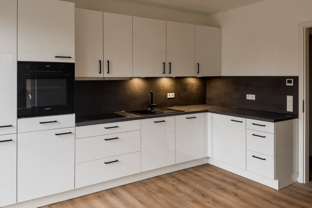 U-förmige Einbauküche mit hellen Schränken, dunkler Arbeitsplatte, Backofen, Dunstabzug und Spüle.