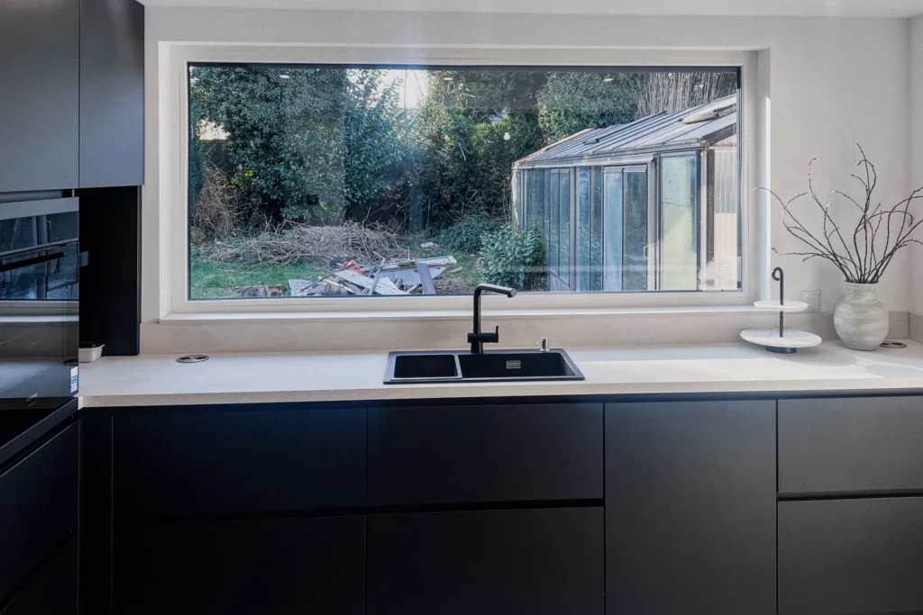 Schwarze Einbauküche mit Spülbecken, Armatur und Fenster über der Arbeitsplatte mit Blick in den Garten