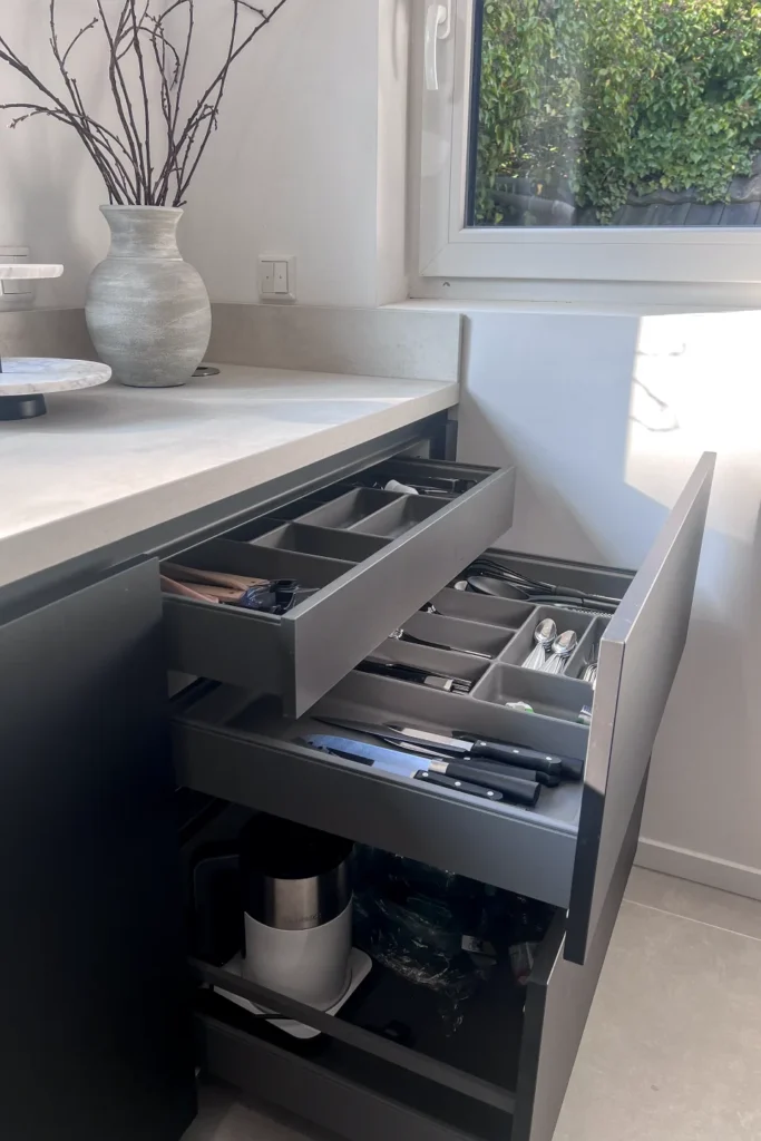 Küchenunterschrank mit geöffneten Schubladen und Besteckeinsatz neben der Fensterbank, helles Design