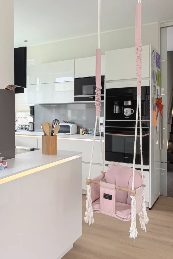 Moderne Küche mit Hochschrank, Einbauherd und rosa Hängeschaukel mit Kissen im Vordergrund