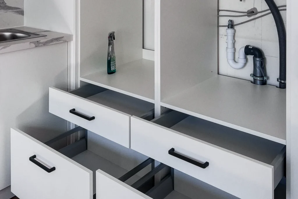 Unterspülschrank mit Schubladen, Flaschenfach und sichtbarer Rohrinstallation unter der Spüle
