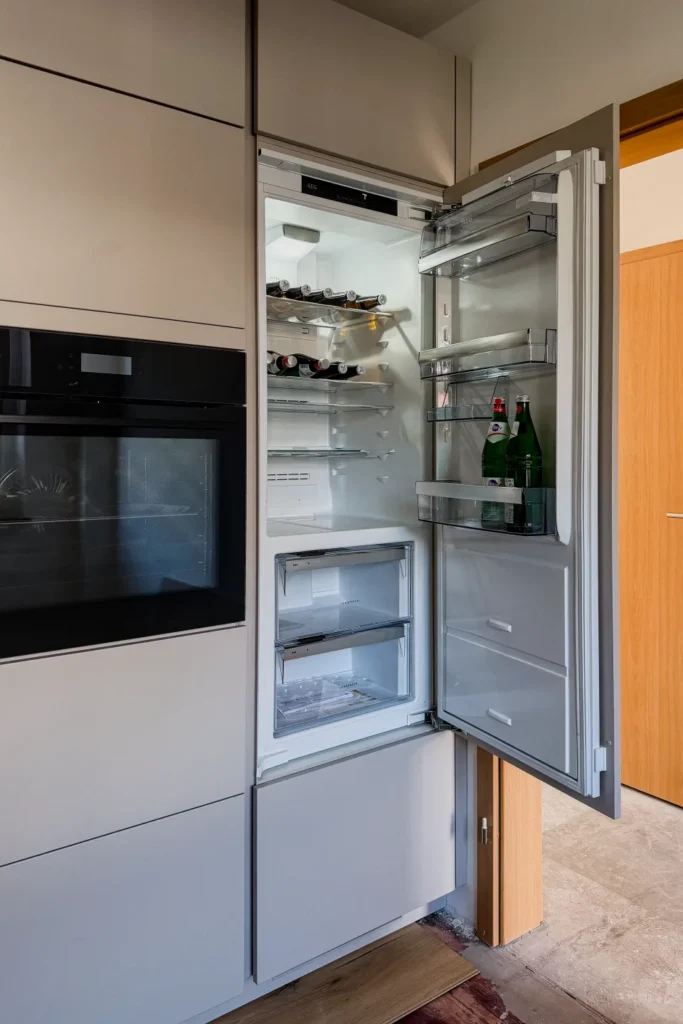 Offener Kühlschrank in der Küchenzeile mit Innenregalen, Flaschen und Gefrierfach