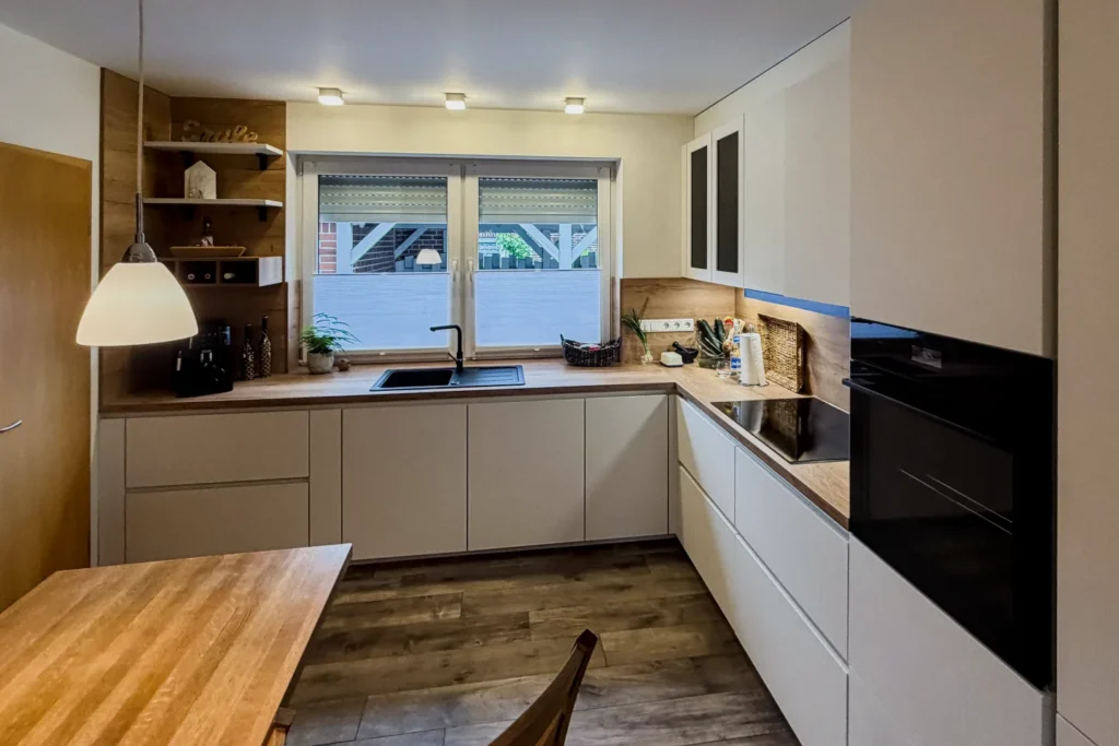 Moderne Einbauküche mit Eckspüle, Schränken, Spülmaschine und Fensterfront im Hintergrund.