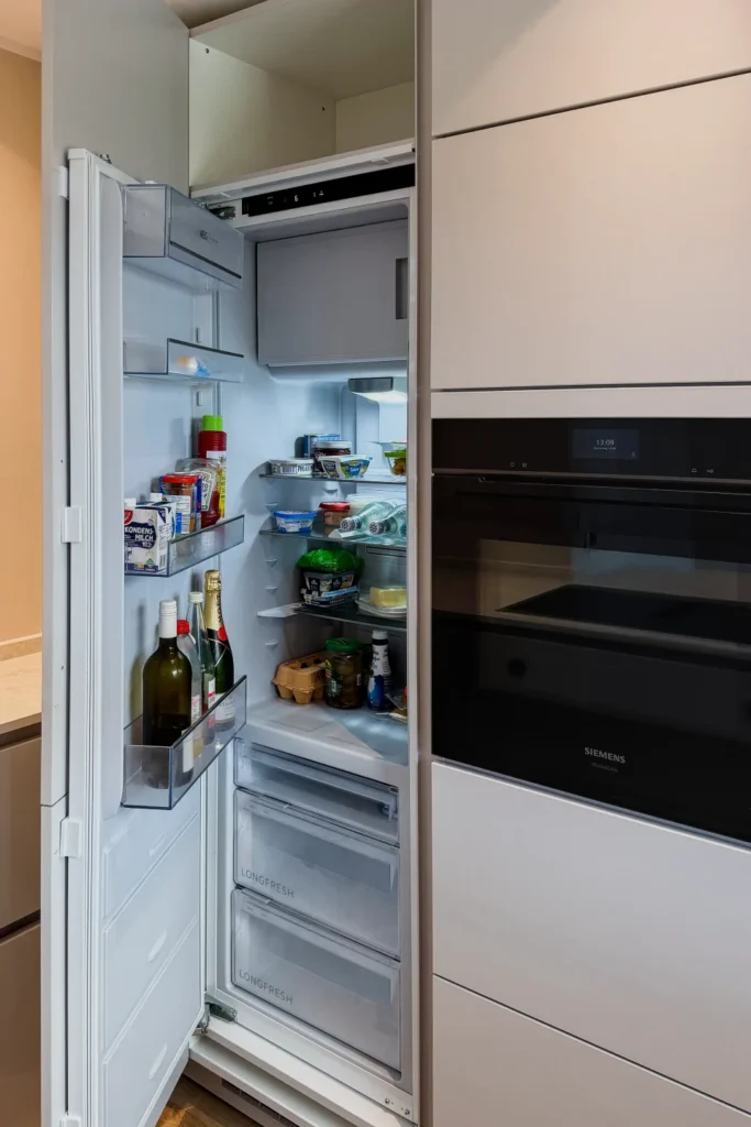 Geöffneter Einbau-Kühlschrank mit Innenregalen und Aufschrift „LONG FRESH“, daneben Einbauherd „SIEMENS“