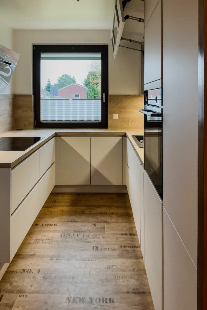 Moderne Einbauküche mit Fronten, Fenster und Arbeitsplatte; auf dem Fußboden steht „NEW YORK“.