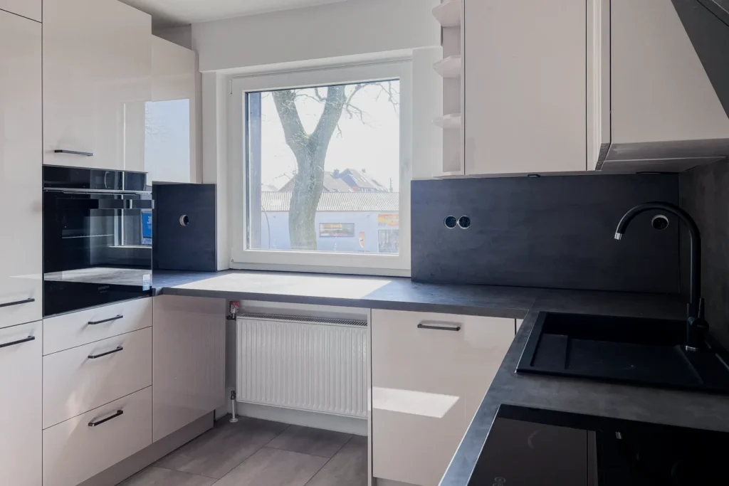 Moderne Küchenzeile mit Einbauherd, Spüle, Oberschränken und Fenster über dem Heizkörper