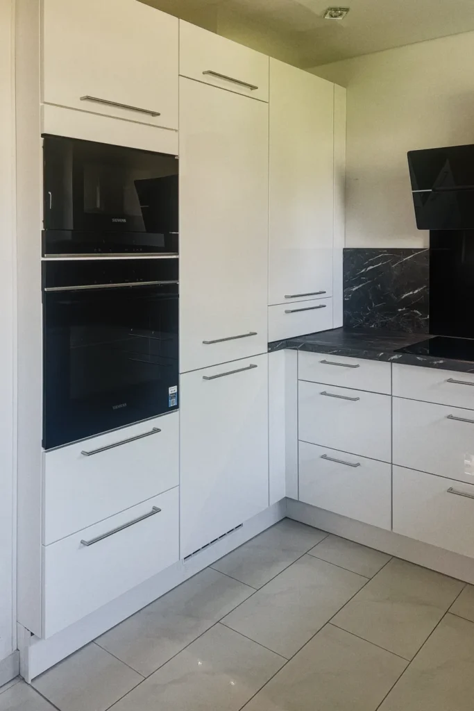 Weiße Einbauküche mit Eckschrank, Schubladen und Backofen; „Siemens“-Aufdruck am Gerät.