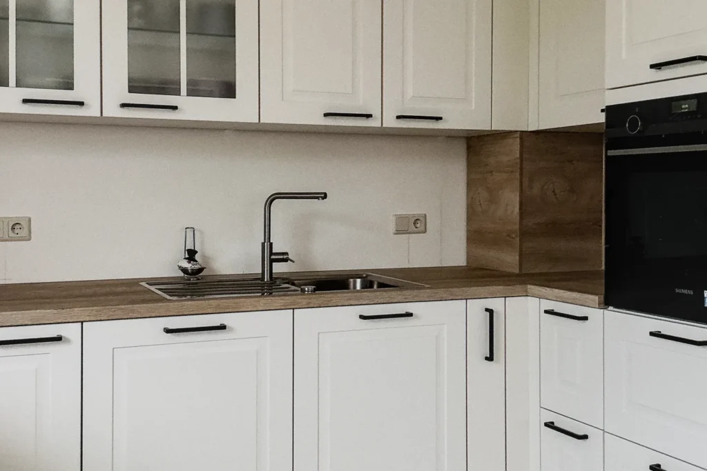 Moderne Küchenzeile mit weißen Fronten, Spüle, Armatur, Nischenrückwand in Holzoptik und Backofen mit „SIEMENS“