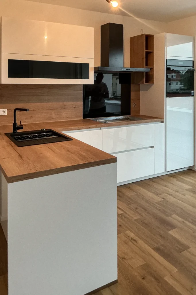 Moderne Einbauküche mit Holz-Arbeitsplatte, weißen Schränken, Spüle und Herd, Dunstabzug über Kochbereich