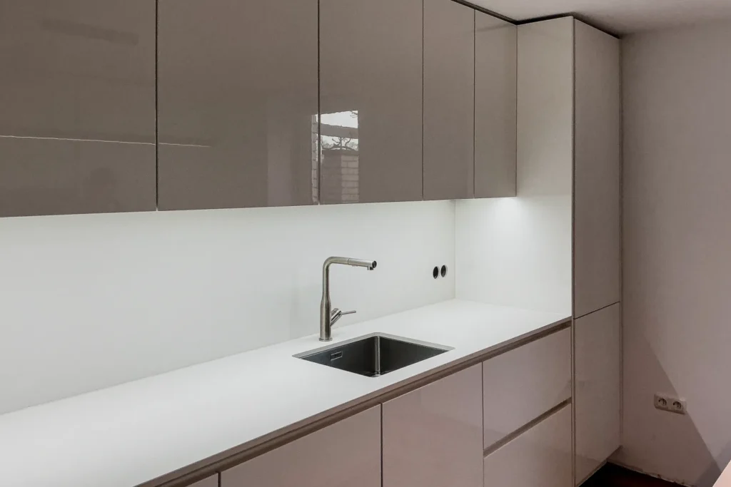 Moderne Küchenzeile mit Oberschränken, Spülbecken und Edelstahlarmatur an der Wand.