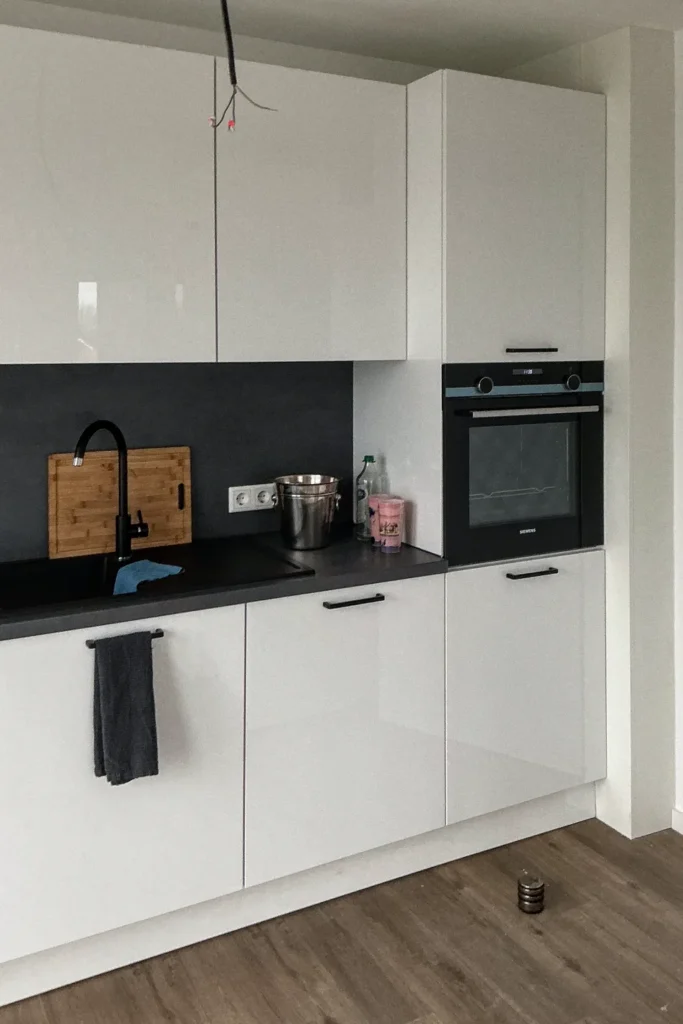 Moderne Küchenzeile mit Spülbecken, Arbeitsplatte und Einbau-Backofen, weißer Schrankfront und Holzbrett am Waschbecken