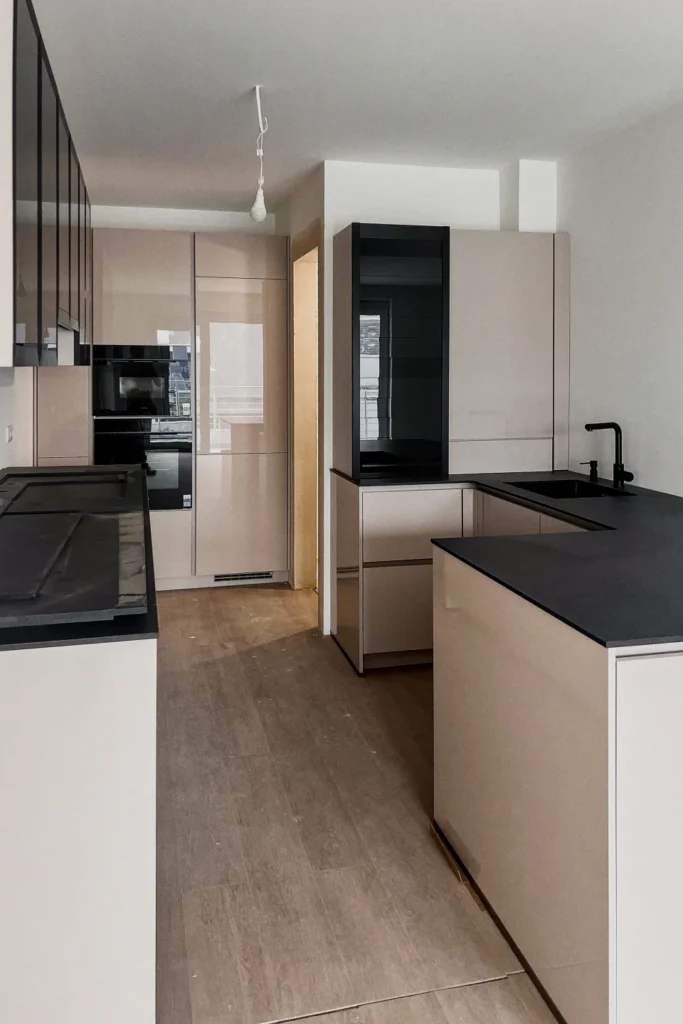 Moderne Küche mit L-förmiger Arbeitsplatte, dunklem Kochfeld, Spüle und hohen Schränken in hellem Design
