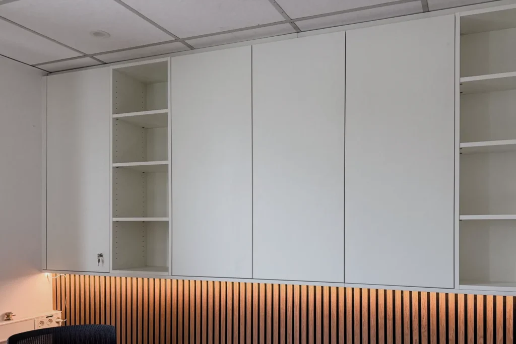Weiße Küchenschränke mit integrierten Regalfächern und Holzleistenverkleidung an der Wand.