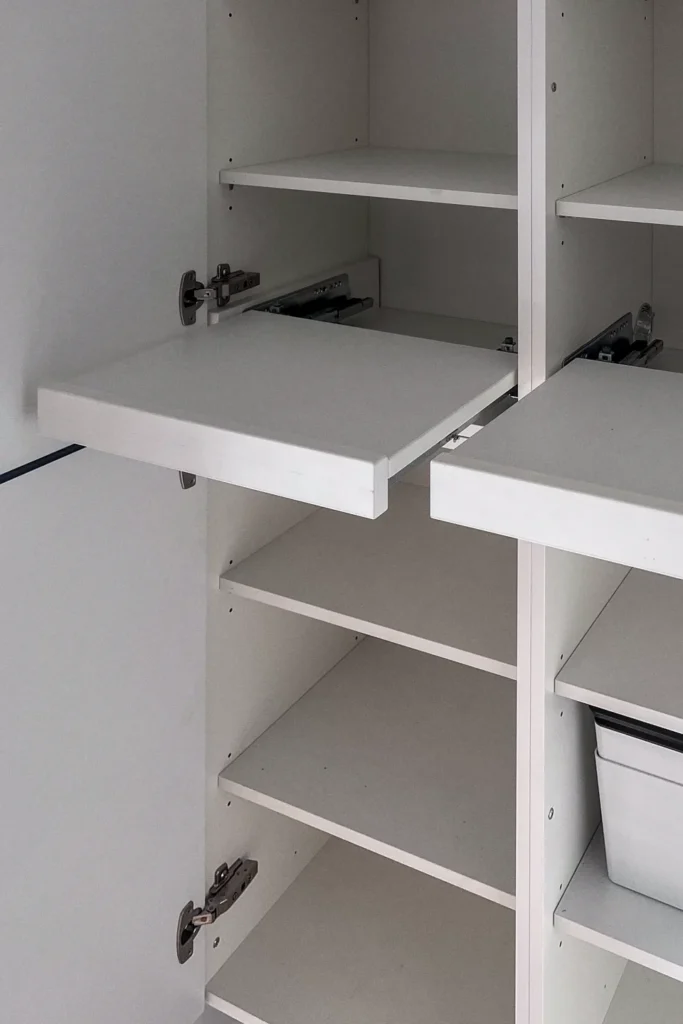 Ausziehbares Küchenschrank-Regal mit geöffneten Klappen und weißen Einlegeböden, darunter Stauraum