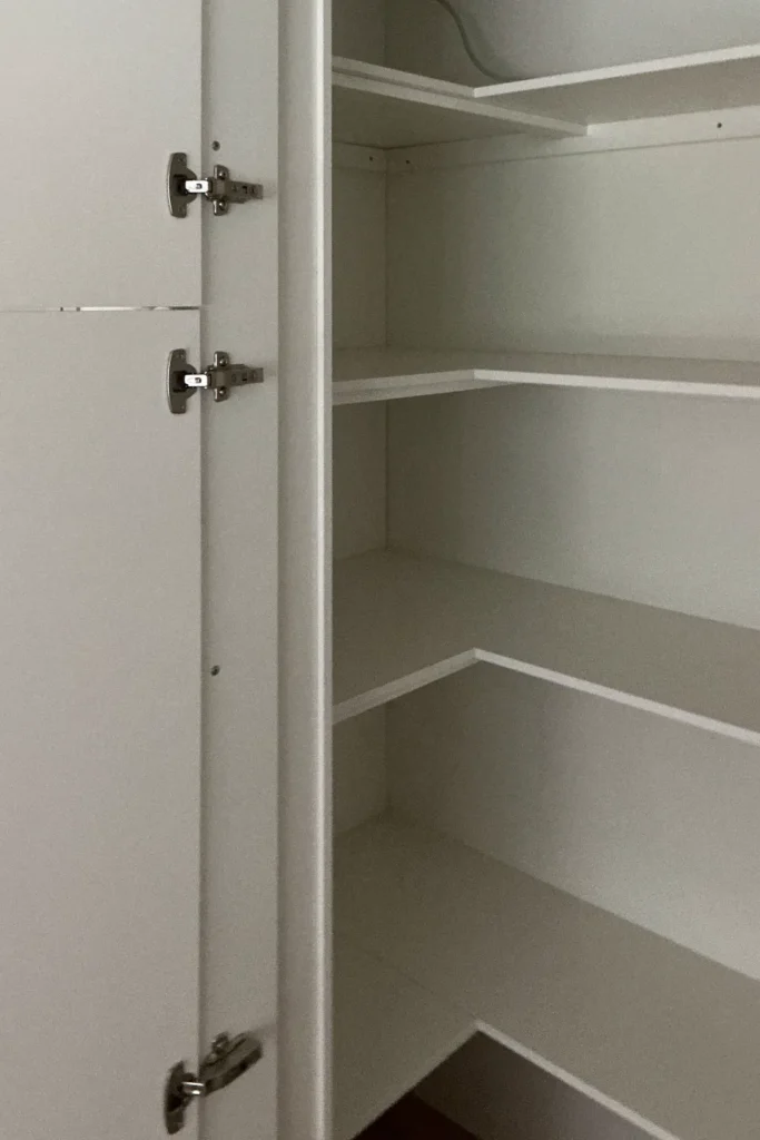 Offener Küchenschrank mit Einlegeböden und Scharnierelementen an der Tür.