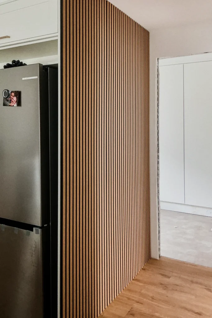 Holzlamellenwand mit Türrahmen, daneben ein Kühlschrank in der Küche
