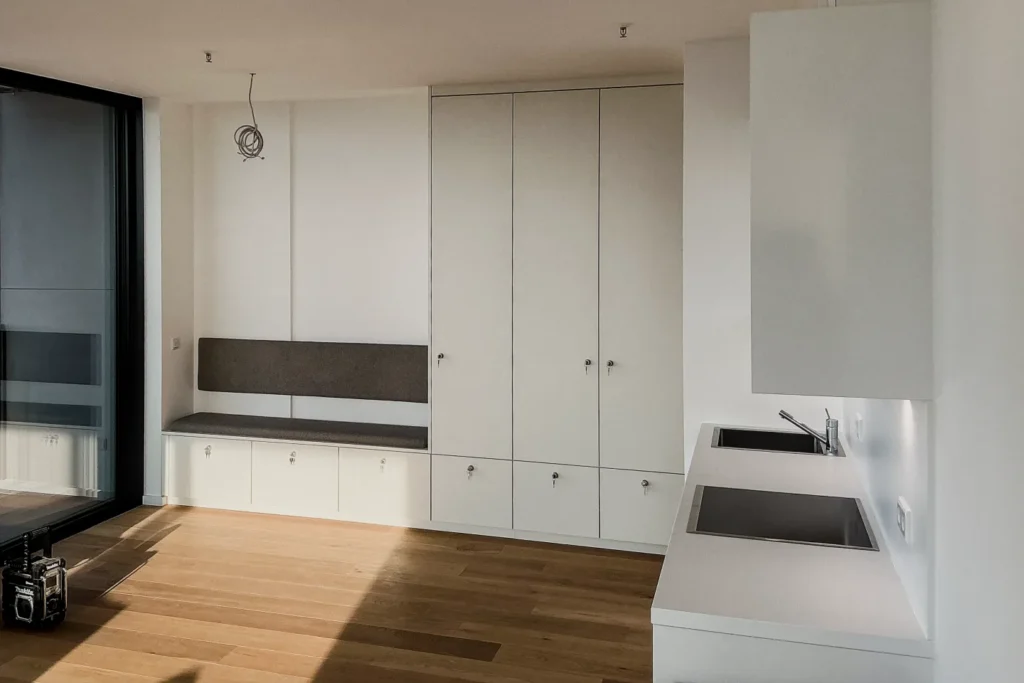 Weiße Küchenzeile mit Hochschrank, integrierter Spüle und Holzarbeitsboden in modernem Raum.