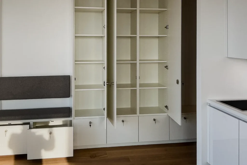 Offener Küchenschrank mit Regalfächern und Schubladen, im Hintergrund ein Sitzbankelement mit Stauraum.