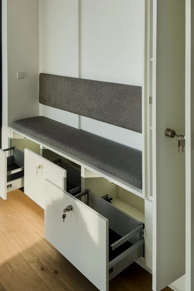 Einbauküche mit grauer Sitzbank und offenen Schubladen unter dem Hochschrank, mit Tür und Griffen.