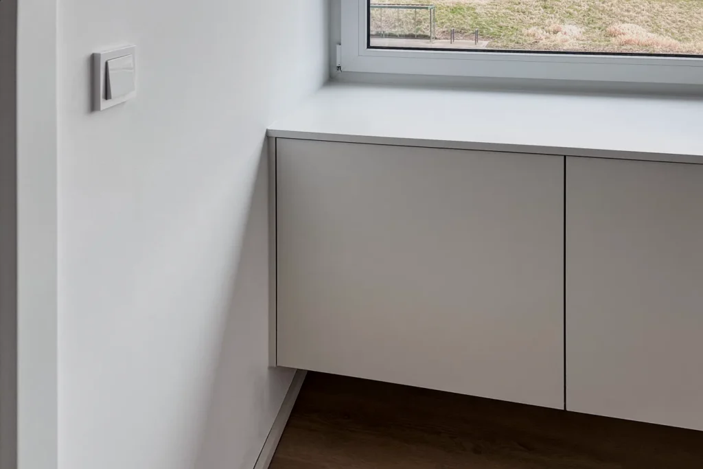 Unterschrank mit zwei Türen unter dem Fenster, in heller Küche an der Wand montiert.