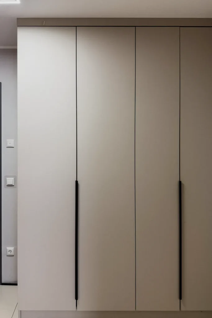 Schrankfront mit vier vertikalen Türen und schmalen Griffen an einer hellen Wand.