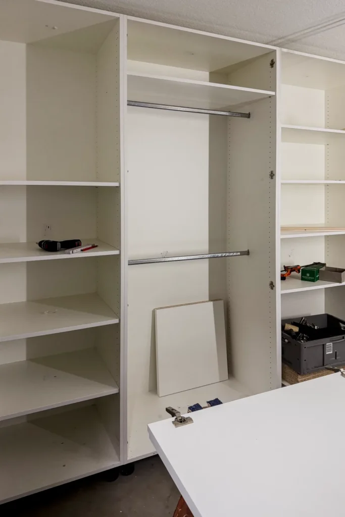 Offener Einbauschrank mit verstellbaren Regalböden und geschlossener Klappe, daneben weiße Arbeitsplatte.