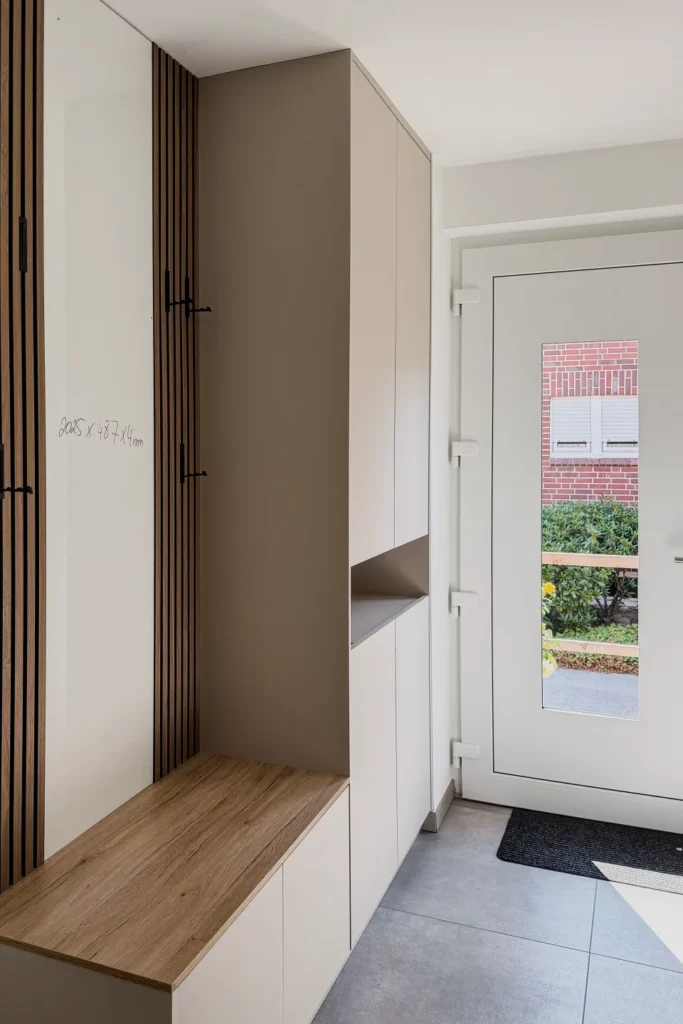 Weiße Garderobe mit Sitzbank und offener Ablage im Flur, Holzboden und rahmenartige Türdetailleisten