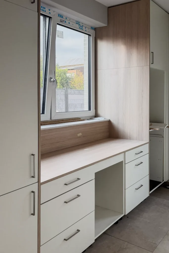 Helle Küchenzeile mit Fensterbank, Schubladen und Einbaumöbeln in Holzoptik und Weiß.
