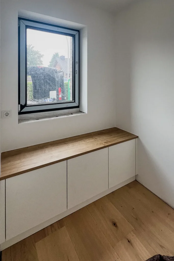 Fenster mit eingebauter Sitzbank und Schrankfronten in der Küche, helle Wände und Holzparkett