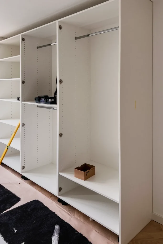 Offener Einbauschrank mit Regalfächern, Schranktüren und Ablageboden, im rechten Bereich mit Karton.