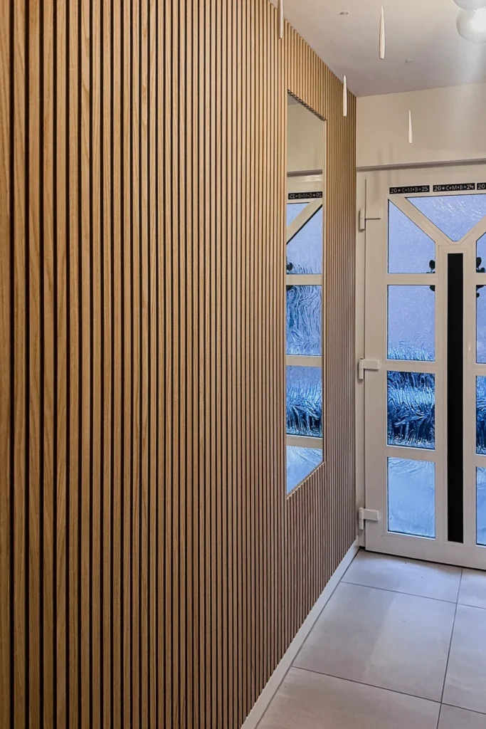 Holzlamellenwand mit Einbaufläche neben einer Glastür im Flur, Blick in den Eingangsbereich
