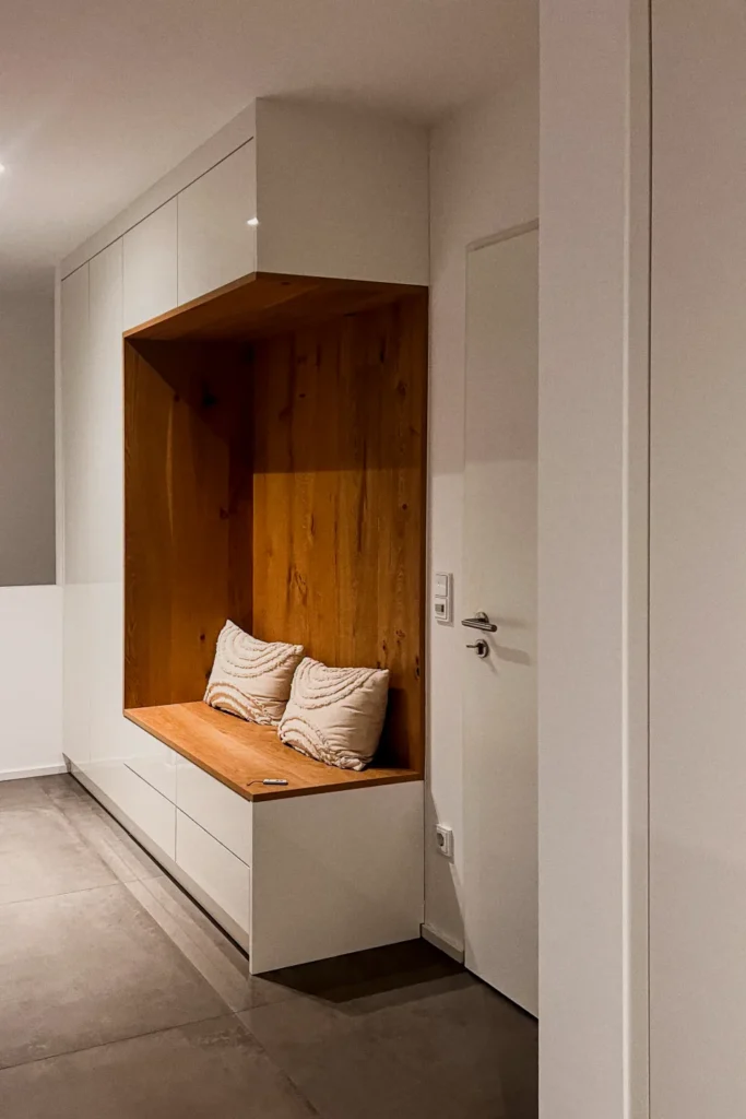 Nische mit Sitzbank aus Holz und weißen Schrankfronten, zwei Kissen, integrierter Stauraum in der Küche.