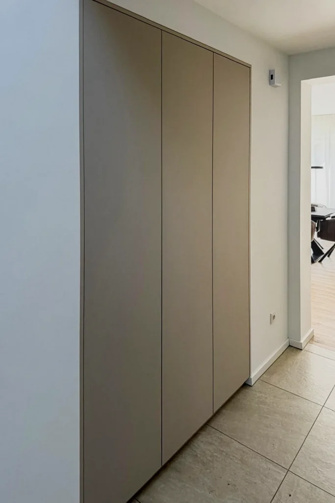 Moderner Einbaukleiderschrank mit rahmenlosen Schiebetüren in einer Flur-Nische, daneben seitliche Wandverkleidung.