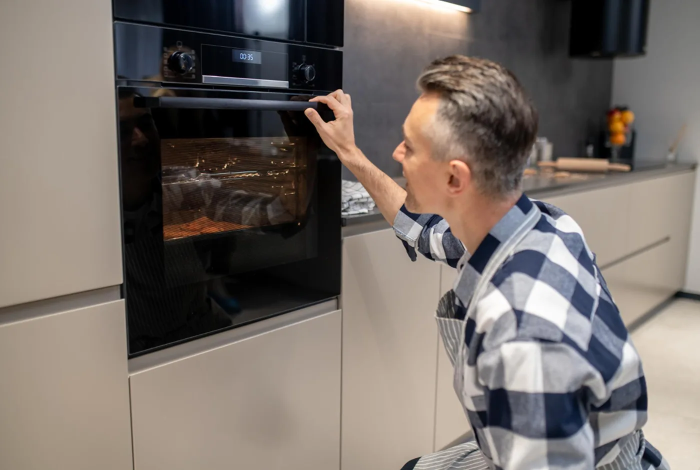 Mann bedient den Einbau-Backofen in einer modernen weißen Küche mit Griff und digitaler Anzeige.