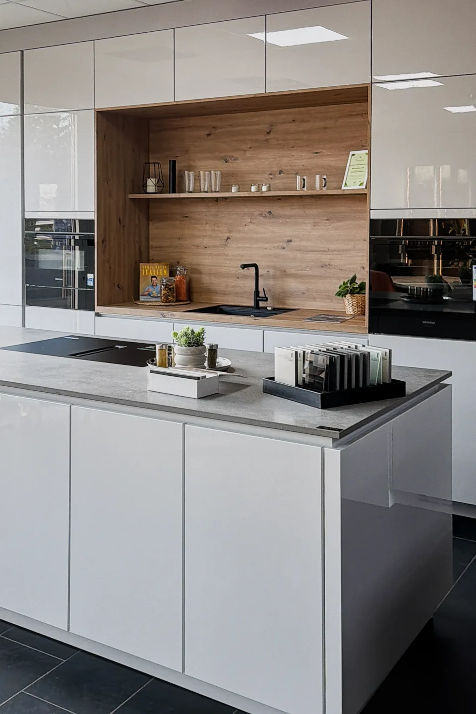 Moderne Küche mit weißem Schrank, Holzrückwand, Arbeitsplatte und Spülbecken mit Wasserhahn.