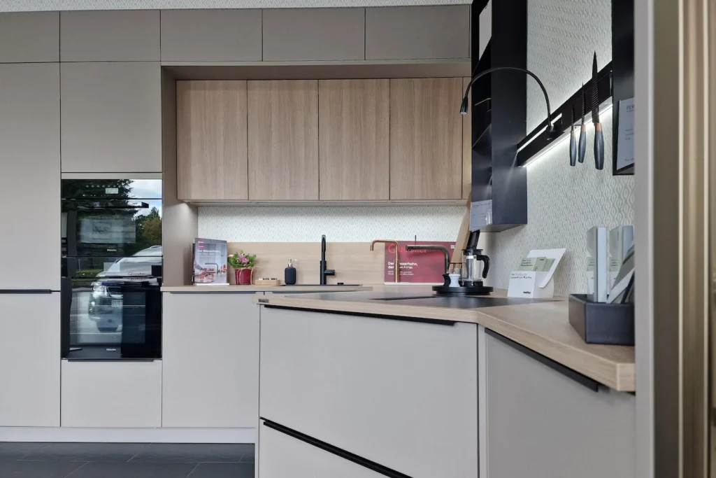 Moderne Küchenzeile mit Spüle, Armatur, Kaffeekanne und Hängeschränken, daneben integrierter Backofen.