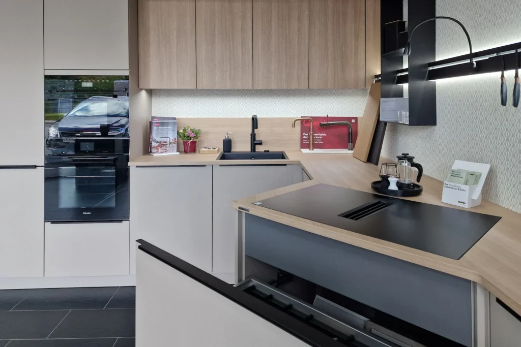 Moderne Küchenzeile mit Holz-Fronten, grauen Schränken, Spülbecken, Induktionskochfeld und Dunstabzug über der Arbeitsplatte.