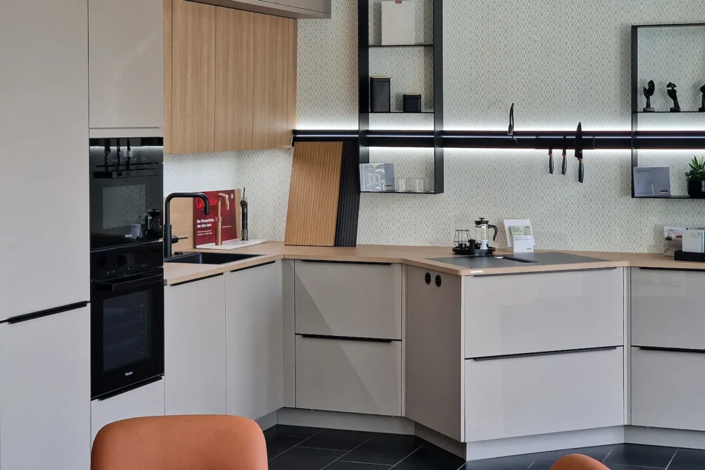Moderne Küchenzeile mit hellen Schrankfronten, schwarzem Backofen, Spüle, Kaffeemaschine und Wandregal.