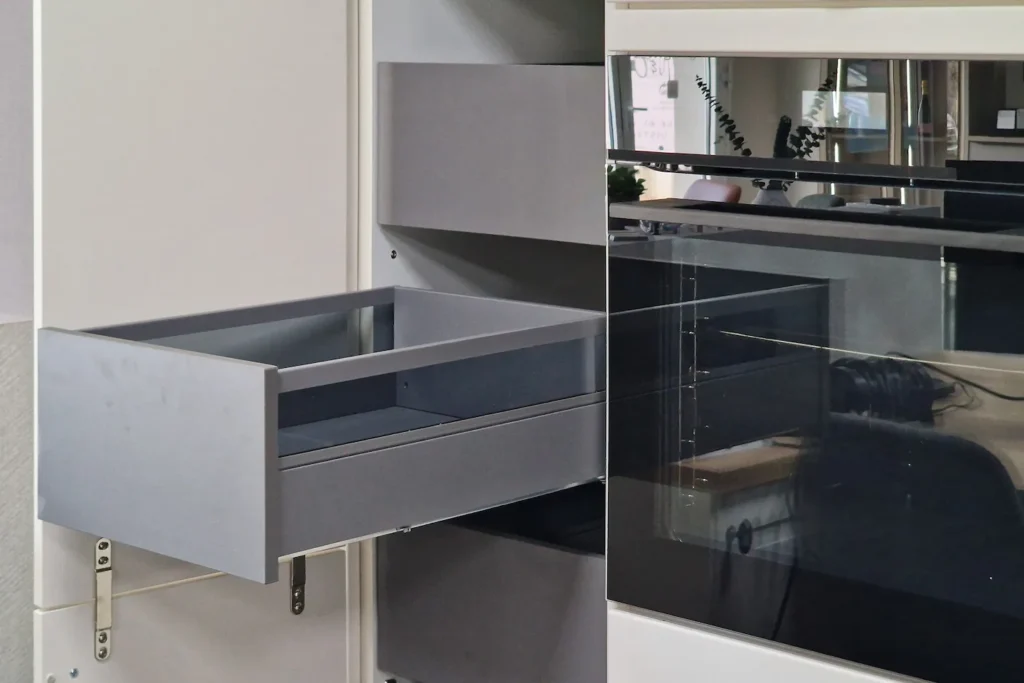 Graue Küchenschublade im geöffneten Unterschrank mit Glastür und eingebautem Küchenbereich
